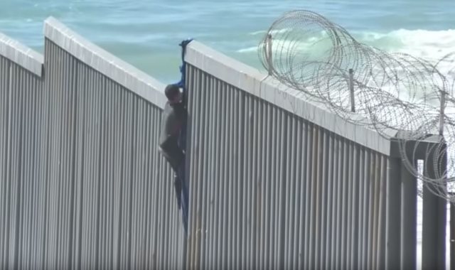 مهاجرون يتسلقون الجدار بين أمريكا والمكسيك