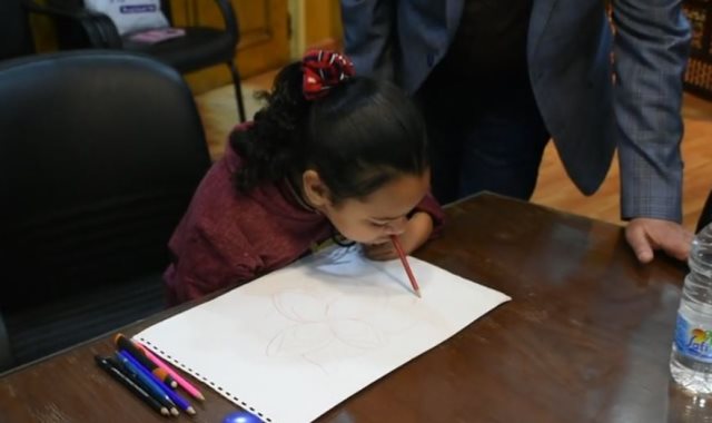 محافظ أسوان يكافئ طفلة مصابة بضمور لموهبتها فى الرسم بـ"فمها"